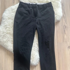 Svarta kostymbyxor med fickor - Svarta kostymbyxor med klassisk rak passform och bälteshällor. Byxorna har sidfickor fram och en bakficka, samt dragkedja och knapp i midjan. Perfekta för en clean och stilren look.