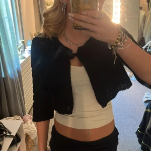 svart bolero  - Säljer en svart stickad bolero från Gina Tricot. den är croppad med trekvartsärmar och knytning framtill. Perfekt att slänga över ett linne för en chill och trendig look. Enkel och stilren design som passar till mycket.