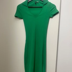 Grön ribbad klänning H&M Divided XXS - Snygg grön ribbad kortklänning från H&M Divided i storlek XXS. Klänningen har v-ringning, krage och korta ärmar. Den är figurnära och stretchig, perfekt för dig som gillar en enkel men trendig look. passar mig som vanligtvis bär xs
