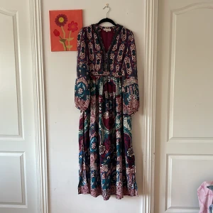 Långklänning från Peru 🇵🇪, Tatienne med pärlor S - Bohemisk långklänning från Tatienne i storlek S. Klänningen har ett färgstarkt mönster i vinrött, blått, grönt och vitt, långa ärmar och v-ringning med handsydda pärldetaljer. Luftigt material, perfekt för dig som gillar unika prints och snygga detaljer. Hela vägen importerad från Peru!🇵🇪 