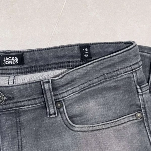 Grå jeansbyxor från Jack & Jones - Snygga grå jeansbyxor från Jack & Jones i en klassisk femficksdesign. Byxorna har en knapp och dragkedja framtill och är tillverkade i ett slitstarkt material. Perfekta för en stilren look. Passar dig som är 170cm ish
