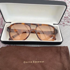 Solglasögon från Corlin Eyewear - Snygga solglasögon från Corlin Eyewear med en klassisk aviatorform. Bågarna har ett stilrent sköldpaddsmönster i brunt och glasen är tonade i en matchande nyans. Perfekta för en solig dag!