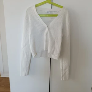 Vit ribbad kofta från Lindex - Säljer en stilren vit ribbad kofta från Lindex. Den har en v-ringad design med knappar framtill och långa ärmar. Perfekt för lager-på-lager under kyligare dagar. Passar till både jeans och kjol!
