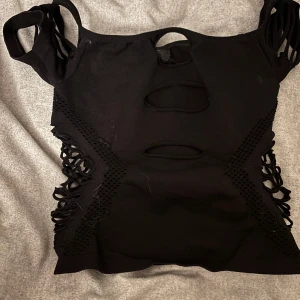 Svart topp med utskärningar - Snygg svart topp med unika utskärningar och detaljer på sidorna och fram. Perfekt för en trendig look. Toppen har korta ärmar och en tight passform.🩷