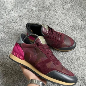 Valentino Rockrunner - Snygga Valentino Rockrunner sneakers i vinrött med svarta detaljer. Skorna har ett coolt kamouflagemönster och är tillverkade i en mix av skinn och mocka. De har en bekväm gummisula och klassisk snörning.Storlek 43 passar 44