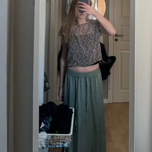 Blommig topp från Lindex - Säljer en färgglad blommig topp från Lindex. Toppen har korta ärmar med volangdetaljer och en söt, croppad passform. Perfekt för att liva upp garderoben med lite färg och mönster!