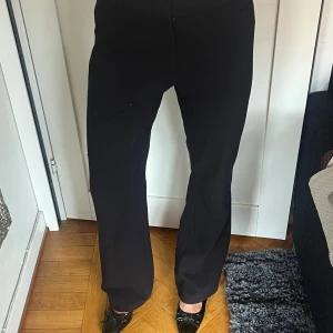 Svarta kostymbyxor - Snygga svarta kostymbyxor med en klassisk passform. De har en rak stil och är perfekta för en stilren look. Byxorna har en midwaist design och är tillverkade i ett bekvämt material.