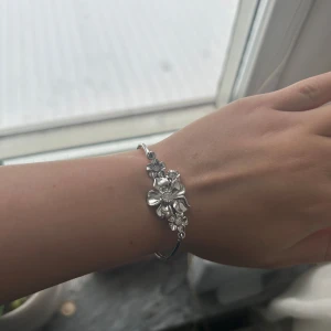  Ioaku Silverfärgat armband med blommor - Elegant silverfärgat armband med vackra blommor som dekoration. Perfekt för att ge en stilfull touch till din outfit. Armbandet har en enkel och tidlös design.