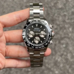 Seiko Daytona Mod Svart - Seiko Mod Daytona är inspirerad av den ikoniska Daytona-designen och utrustad med den prestigefyllda Seiko VK63 hybridrörelsen. Denna 40 mm klocka kombinerar elegans och funktionalitet med hög tillgänglighet.  Funktioner: • Diameter: 40 mm (utan krona) • Rörelse: Seiko VK63 hybrid (automatisk + kvarts) • Tjocklek: 12 mm • Glas: Safir, rep-resistent • Luminova: Ja • Material: 316L rostfritt stål • Bezel: Keramik • Armband: 316L stål med säkerhetslås • Vattentålig: 3 ATM • Fungerande kronograf: Ja
