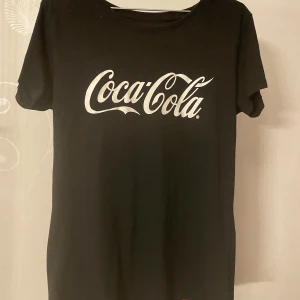 Coca-Cola t-shirt i svart och vit - Två coola Coca-Cola t-shirts, en i svart med vit logga och en i vit med röd logga. Perfekta för en avslappnad stil med korta ärmar och klassisk passform. Visa din kärlek för den ikoniska drycken med dessa stilrena plagg!