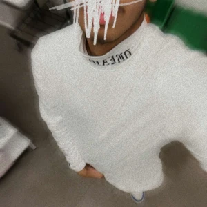 Vit långärmad tröja med text på kragen - Säljer en stilren vit långärmad tröja med textdetalj på kragen. Perfekt för en minimalistisk look. Passar bra till både jeans och chinos.