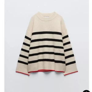 Beige och svart randig stickad tröja - Säljer en mysig beige stickad tröja med svarta ränder och röda detaljer vid ärmslut och nederkant. Tröjan har en avslappnad passform och långa ärmar, perfekt för kyligare dagar.