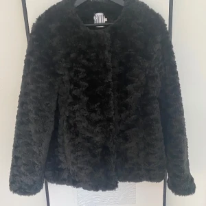 Svart teddy jacka/ fuskpäls från Saint Tropez - Snygg och fluffig svart jacka från Saint Tropez i storlek M. Jackan har en mjuk och lyxig känsla med knappar framtill. Perfekt för att hålla sig varm och stilren under kyliga dagar.