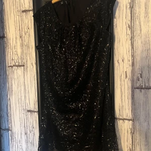 Svart glittrig klänning från Zay - Snygg svart klänning från Zay med glittrande paljetter som ger en festlig look. Klänningen har en elegant design med korta ärmar och en rund hals. Perfekt för att sticka ut på festen! ✨