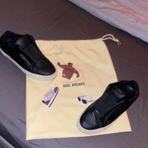 Svarta sneakers från Axel Arigato - Snygga svarta sneakers från Axel Arigato med en stilren design. Skorna har en vit sula och är tillverkade i skinn. Perfekta för en minimalistisk look.