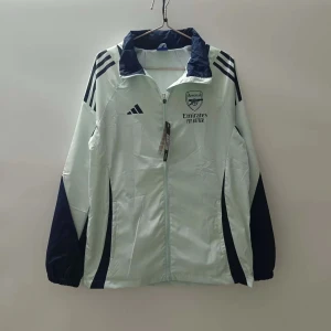 Arsenal jacka - Säljer en stilren vit och marinblå vindjacka från Adidas med dragkedja och klubbmärke på bröstet. Jackan har långa ärmar och sportig design med mörka detaljer på sidorna och axlarna.