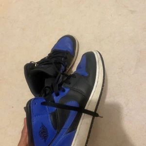 Svart och blå Nike Air Jordans - Snygga Nike Air Jordans i svart och blått. Skorna har en klassisk design med snörning och den ikoniska Air Jordan-loggan på sidan. Perfekta för dig som vill ha en stilren och sportig look.