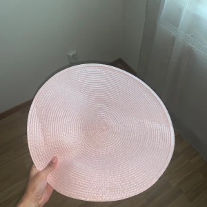 Rosa  bordstabletter - Säljer två rosa bordstabletter i flätat material. Perfekta för att ge ditt bord en elegant touch. De är runda och har en subtil textur som ger en fin detalj till dukningen.