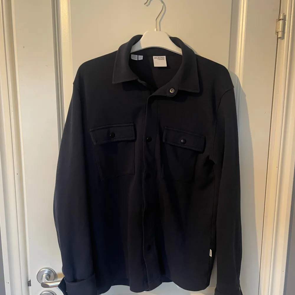 Säljer en stilren mörkblå overshirt från Selected Homme. Den har långa ärmar och knappar framtill samt två bröstfickor med knappar. Perfekt för vår, sommar och höst!. Takit.