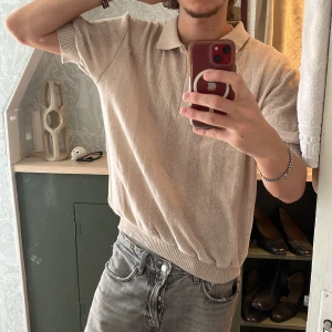 Beige pikétröja från Družena - Säljer en stilren beige pikétröja från Družena. Tröjan har korta ärmar och en klassisk krage med knappar framtill. Perfekt för en avslappnad och snygg look. Passar bra till jeans eller chinos.