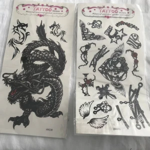 Tillfälliga tatueringar med drakar och dödskallar - Säljer ett set med tillfälliga tatueringar. Första arket har en stor svart drake och tribal-mönster. Andra arket innehåller dödskallar, rosor och ankare i svartvitt. Tredje arket har färgglada drakar i rött, blått och grönt. Perfekt för att testa olika stilar utan att binda sig permanent. 25kr/st . Sammafrakt 