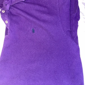 Lila pikétröja från Ralph Lauren - Säljer en snygg lila pikétröja från Ralph Lauren med klassisk krage och knappar framtill. Tröjan har korta ärmar och det ikoniska broderade logotypen på bröstet. Perfekt för en stilren look! Den är stor i storleken skulle säga att den passar XL passar någon som är stor i kroppen 