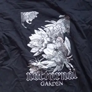 Snygg svart t-shirt med ett stort blommigt tryck och texten 'nocturnal garden' på framsidan. Välanvänd och därför lite rynklig men det är det enda defekten som kan strykas bort