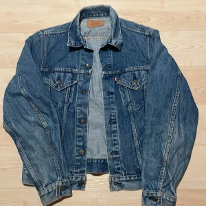 Vintage jeansjacka från Levi's - Klassisk blå jeansjacka från Levi's med knappar framtill och två bröstfickor. Perfekt för en avslappnad stil. Jackan har en normal passform och långa ärmar.