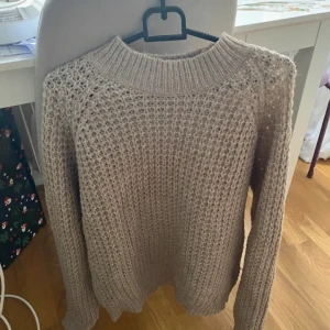 Beige stickad tröja - Säljer en mysig beige stickad tröja med långärmad design. Perfekt att dra på sig över linnet på sommarkvällar.  Bekväma passform. Tröjan har en klassisk rund hals och ribbstickade muddar vid ärmslut och nederkant.