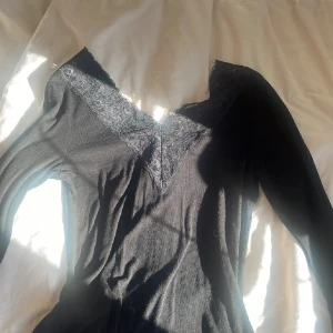 Svart långärmad topp med spetsdetaljer - Snygg svart långärmad topp med v-ringad spetsdetalj. Säljer vidare då den svarta färgen inte passade mig.