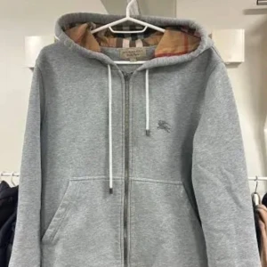 Grå hoodie från Burberry - Säljer en stilren grå hoodie från Burberry med dragkedja och justerbar huva. Insidan av huvan har det klassiska Burberry-mönstret. Perfekt för en avslappnad look.