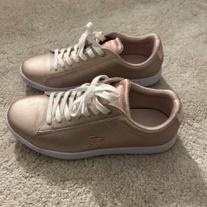  sneakers från Lacoste , ROSÉ  - Snygga rose sneakers från Lacoste med vita snören och en diskret krokodil-logga på sidan. Skorna har en stilren design med en vit sula som ger en fräsch look. Använt endast 1 gång sen bara legat hemma, fräscha och FINT skick. Köpta för 1299 säljs nu för 299, pris går att diskutera🥰