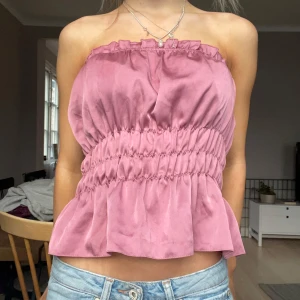 Rosa axelbandslös topp - Säljer en söt rosa axelbandslös topp med volangdetaljer. Toppen har en elastisk midja som ger en fin passform och en luftig nederdel. Jätte bra skick!!💘