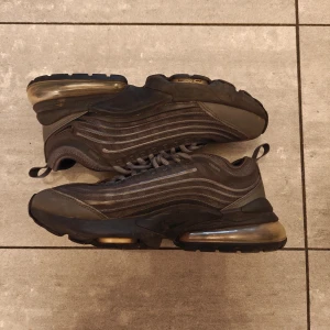 Svarta Nike sneakers - Snygga svarta Nike sneakers med synlig Air Max-dämpning i sulan. Skorna har en modern design med svarta snören och en diskret Nike-logga i orange på hälen.