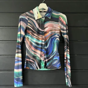 Flerfärgad skjorta från BikBok - Säljer en cool flerfärgad skjorta från BikBok med abstrakt mönster i blått, rosa, grönt och svart. Skjortan har långa ärmar och knappar framtill. Perfekt för dig som vill sticka ut med en unik stil!