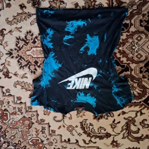 Svart och blå ärmlös topp från Nike - Säljer en cool svart och blå ärmlös topp från Nike med ett stort vitt logotryck på framsidan. Perfekt för en avslappnad stil eller träning. Toppen har ett unikt mönster som ger en extra touch.