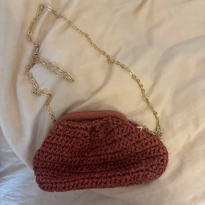 Röd  axelväska med kedja - Snygg röd axelväska med en elegant guldkedja som axelrem. Väskan har en unik stickad design som ger den en bohemisk känsla. Perfekt för att ge din outfit en extra touch av stil. ENDAST AMVÄND EN GÅNG!!