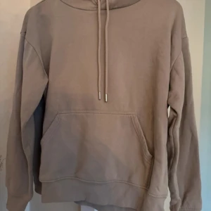 Beige hoodie med ficka - Säljer en stilren beige hoodie med känguruficka och justerbar dragsko i huvan. Perfekt för en avslappnad look. Passar bra till både jeans och mjukisbyxor.
