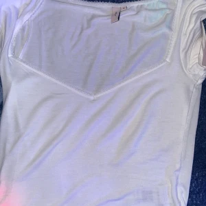 Vit kortärmad topp - Säljer en stilren vit topp med korta ärmar och en v-ringad design. Perfekt för en enkel och snygg look. Passar bra till jeans eller kjol för en avslappnad stil.