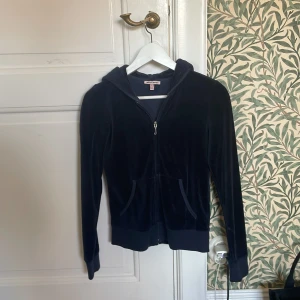 Svart velourjacka från Juicy Couture - Säljer en snygg svart velourjacka från Juicy Couture med dragkedja och huva. Jackan har ett stort tryck med text och krona på ryggen. Perfekt för en avslappnad och trendig look.❤️