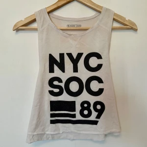 Vit linnetopp från SOC - Säljer en vit linnetopp från SOC med svart text på framsidan. Toppen har en rund halsringning och är ärmlös.