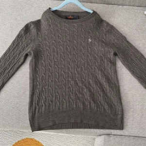 Brun kabelstickad tröja från Gant - Merinoulltröja från Morris – som ny! Säljer en stilren och klassisk grå tröja i 100% merinoull från Morris. Den har ett fint kabelstickat mönster och diskret logga på bröstet. Supermjuk, varm och perfekt till både vardag och lite mer uppklätt.  Storlek: S (passar även XS) Skick: Väldigt fint skick, sparsamt använd Pris: 400 kr  Nypris runt 1600 kr. Hör av dig vid frågor!