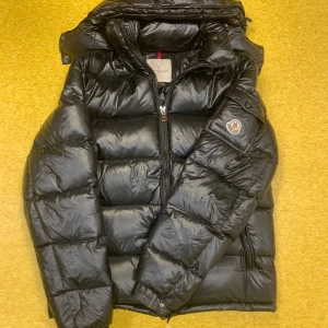 Moncler Maya - Säljer en snygg svart pufferjacka från Moncler.  har en glansig yta med dragkedja och Moncler-logga på ärmen. Perfekt för kyliga dagar med sin varma och stilrena design. Storlek 3 passar bra ifall man har storleken M/L!