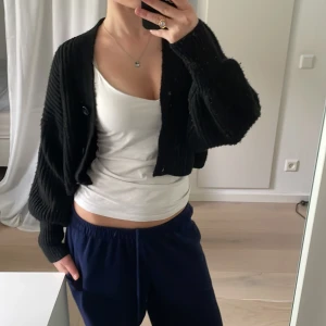 Svart ribbad kofta från Gina Tricot - Säljer en svart ribbad kofta från Gina Tricot. Koftan har en croppad passform med knappar framtill och långa ärmar. Perfekt för lager-på-lager-stil. 🖤