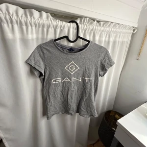 Grå t-shirt från GANT - Säljer en grå t-shirt från GANT med korta ärmar och ett tryck av GANT-loggan på framsidan. Perfekt för en avslappnad stil. Passar bra till jeans eller shorts.