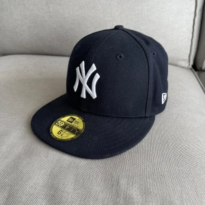 Mörkblå från New Era - Snygg mörk blå keps från New Era med vit broderad logga framtill och texten ”PREDATORN” på sidan. Kepsen är en 59FIFTY-modell med en platt skärm och är i storlek 6 7/8. Bara testat storleken aldrig använd annars.