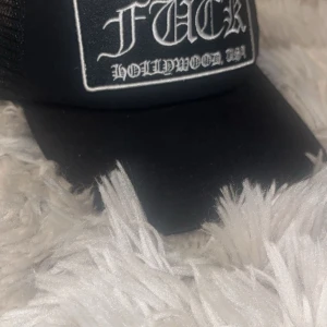 Svart keps från Chrome Hearts - Snygg svart keps från Chrome Hearts med texten 'F*** Hollywood USA' framtill. Kepsen har ett nätmaterial baktill och en justerbar rem för perfekt passform. Perfekt för en cool och avslappnad stil.