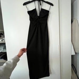 Svart klänning från Gina Tricot - Säljer denna perfekta svarta sommarklänning från Gina Tricot! Modellen är knälång med ett justerbart band som knyts i nacken för att hålla klänningen på plats. De tunna “spaghetti strapsen” är bara för upphängning – inte till för att bäras över axlarna. Skriv om ni har frågor!💕