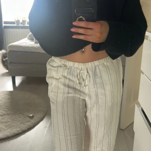 Linnebyxor  - Snygga vita byxor med svarta ränder och bekväm snörning i midjan. Byxorna har en avslappnad passform och är perfekta för en stilren look. De har också praktiska fickor baktill.