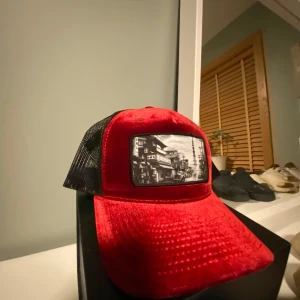 Röd och svart keps med motiv - Snygg keps i röd och svart med ett coolt svartvitt motiv på framsidan. Kepsen har ett nätmaterial baktill för bra ventilation och en böjd skärm. Perfekt för en avslappnad stil.